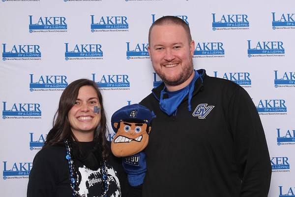Two alumni holding up Louie the Laker puppet